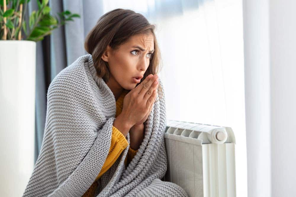 cold woman in a blanket sit beside a heating radiator