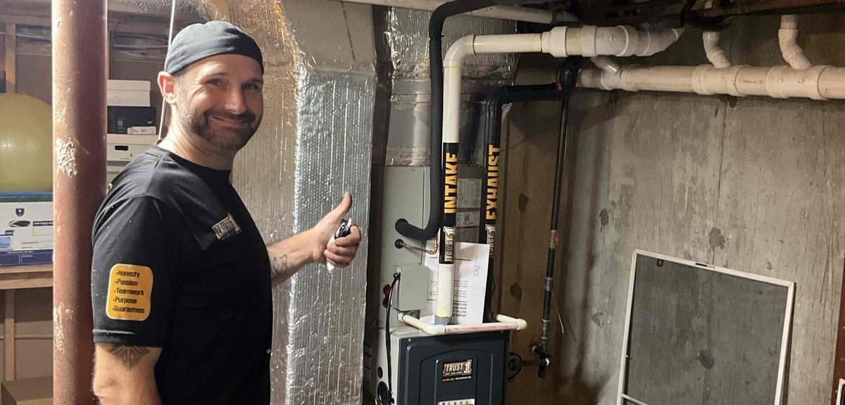 Trust 1 technician giving a thumbs-up beside a newly installed American Standard furnace